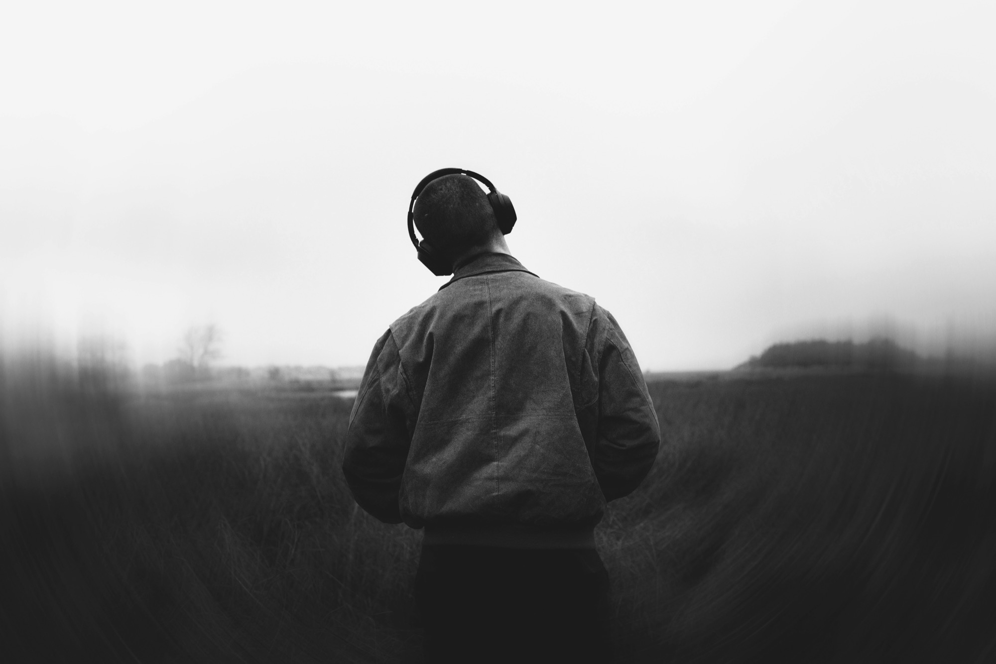A man standing in a field wearing headphones, seen from behind
